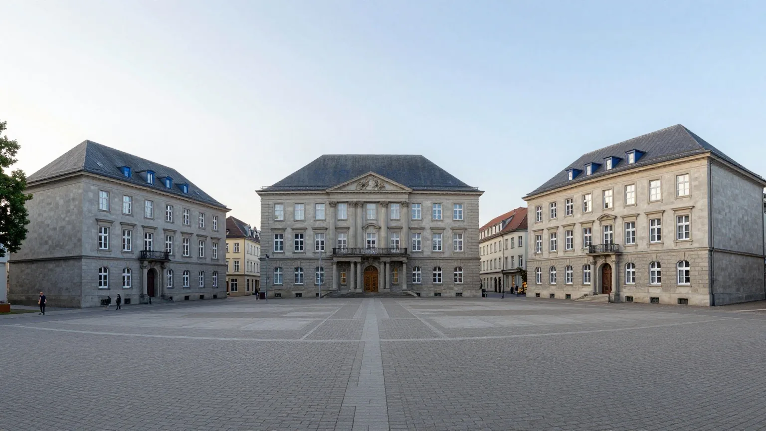 Drei getrennte Steingebäude an einem ruhigen Platz in einer deutschen Stadt, verbunden durch gepflasterte Wege