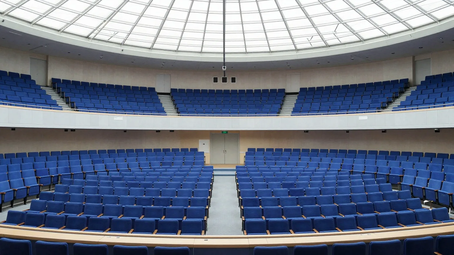 Ein großer halbrunder Plenarsaal mit leeren blauen Sitzreihen, von der oberen Tribüne aus gesehen