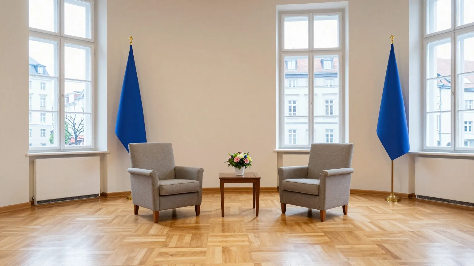 Ein festlicher Empfangsraum mit Parkettboden, zwei leere Sessel an einem kleinen Tisch mit Blumen im Nachmittagslicht